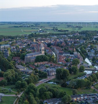 Aerial view of the historic town of Bolsward with its prominent church, winding canals, and surrounding green landscape under a soft evening sky in Bolsward, Friesland, Netherlands.