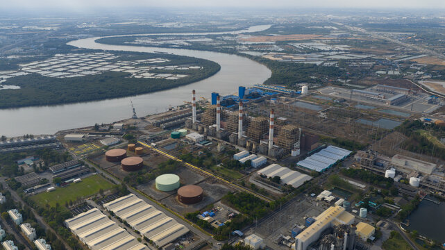 Aerial view of the Tha Kham power plant facility with its tall chimneys, storage tanks, and industrial buildings situated along the river in Bangkok, Thailand.