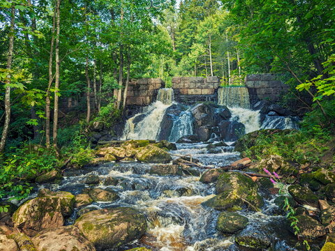 Espoo, Finland - 01.08.2020: Small waterfall cascading over a stone dam into a rocky forest stream under bright summer sunlight