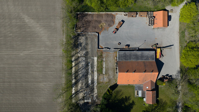 Aerial view of a farm complex with an orange-roofed building, a tractor in the yard, and adjacent agricultural fields in Luttelgeest, Flevoland, Netherlands.