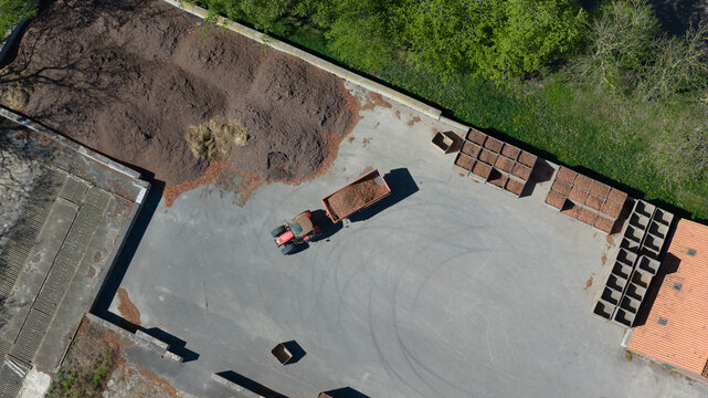 Aerial view of a tractor with a trailer loaded with organic material in an agricultural yard with crates and piles of mulch in Luttelgeest, Flevoland, Netherlands.
