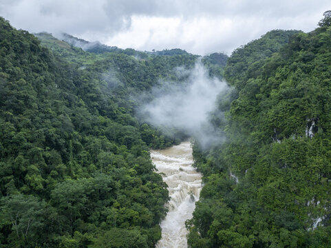 Aerial view of Semuc Champey featuring the Cahabon River flowing through a lush tropical rainforest canyon under a cloudy sky in San Agustin Lanquin, Alta Verapaz, Guatemala.