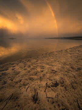 View of Princess Royal Harbour at sunset with a rainbow arching over the calm water and sandy shoreline in Albany, WA, Australia.