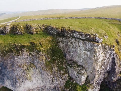 Aerial view of the limestone cliffs and grassy slopes of Winnats Pass with a stone wall along the ridge in Hope Valley, England, United Kingdom.