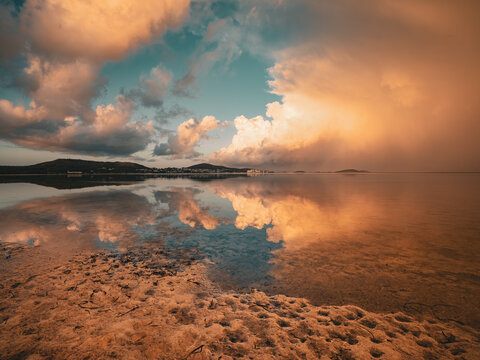 View of Princess Royal Harbour at sunset with dramatic golden clouds reflecting on the calm water and a textured shoreline in Albany, WA, Australia.