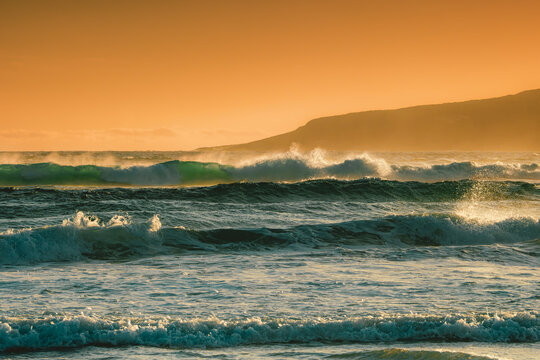 View of Anvil Beach with waves crashing against the shore under a warm golden hour sky in Nullaki, Western Australia, Australia.