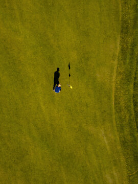 Aerial view of a golfer putting on a green with a flagstick and long shadow cast on the grass, Baden-Wurttemberg, Germany.