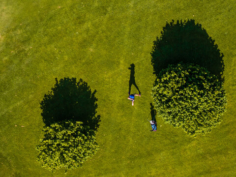 Aerial view of a golfer walking on a green grass golf course with trees casting long shadows in Baden-Wurttemberg, Germany.