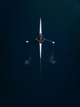 Aerial view of a single rower in a sculling boat gliding across dark water in Mannheim, Baden-Wurttemberg, Germany.