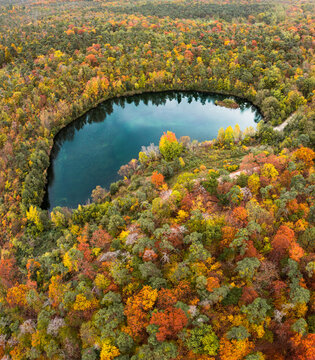 Aerial view of a serene lake nestled within a dense forest displaying vibrant autumn foliage with shades of orange, yellow, and red in Mannheim, Baden-Wurttemberg, Germany.