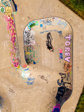 Aerial view of a person riding a bicycle in a concrete skatepark bowl covered in colorful graffiti in Mannheim, Baden-Wurttemberg, Germany.