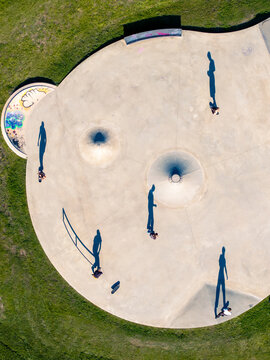 Aerial view of a concrete skatepark in Mannheim with skateboarders casting long shadows on the smooth surface, surrounded by green grass in Mannheim, Baden-Wurttemberg, Germany.