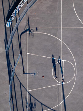 Aerial view of two people playing basketball on an outdoor court with long shadows cast on the grey surface in Mannheim, Baden-Wurttemberg, Germany.