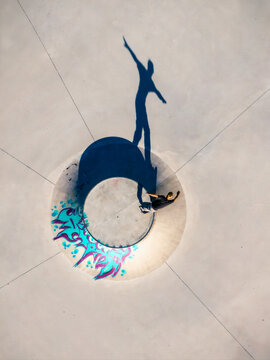Aerial view of a skateboarder in a concrete bowl with colorful graffiti art and a long shadow cast on the ground in Mannheim, Baden-Wurttemberg, Germany.