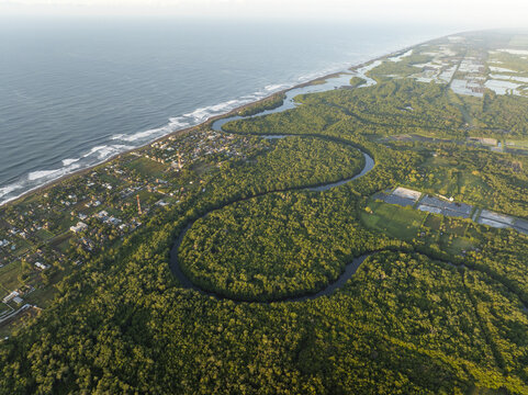 Aerial view of the winding river flowing through lush mangroves and the coastal village of El Paredon along the Pacific Ocean in El Paredon, Escuintla Department, Guatemala.