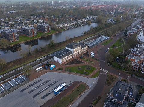 Aerial view of the historic railway station featuring distinctive brick architecture, adjacent canal, surrounding urban area, and bus terminal in the foreground Sneek, Friesland, Netherlands.