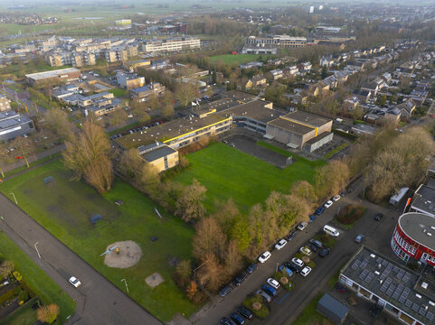 Aerial view of a school building complex with a central green courtyard, surrounding parking areas, and residential streets in Sneek, Friesland, Netherlands.