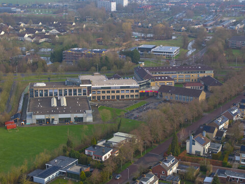 Aerial view of a school complex surrounded by residential houses, green spaces, and trees in Sneek, Friesland, Netherlands.