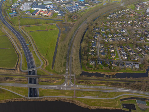 Aerial view of a highway, railway line, and canal intersecting through a residential area and green fields in the Netherlands.