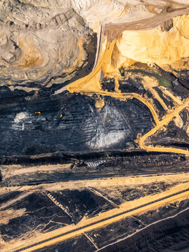 Aerial view of an open-pit coal mine showing layers of dark coal and yellow sand excavation with heavy machinery in North Rhine-Westphalia, Germany.