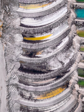 Aerial view of the terraced walls of an open-pit mine showing layers of rock, soil, and vibrant mineral deposits in North Rhine-Westphalia, Germany.