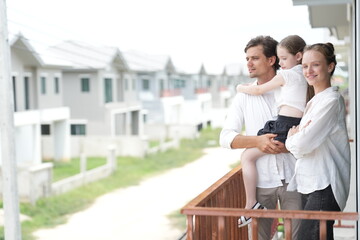 Obraz premium Happy young family with little daughter look out over the rows of new white houses from the railing standing on the terrace of a newly built suburban home, shallow depth of field