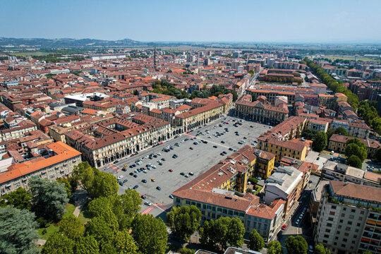 Aerial view of Piazza della Liberta with parked cars surrounded by historic buildings and terracotta rooftops in Alessandria, Piedmont, Italy.