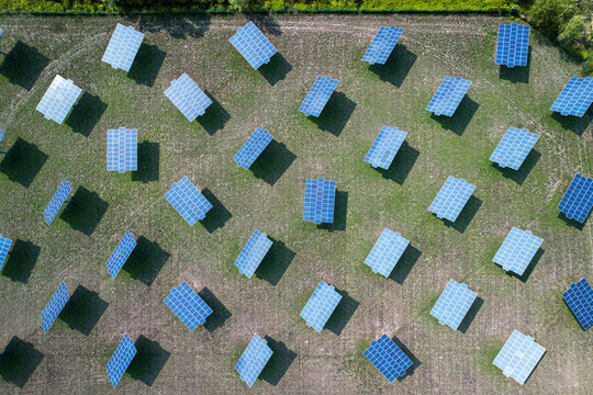 Aerial view of a solar farm with rows of photovoltaic panels installed in a green field in Quattordio, Piedmont, Italy.