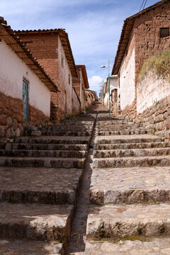 View of the historic stone staircase in the village of Chinchero, flanked by traditional adobe houses with tiled roofs under a clear blue sky in Cusco, Cusco, Peru.