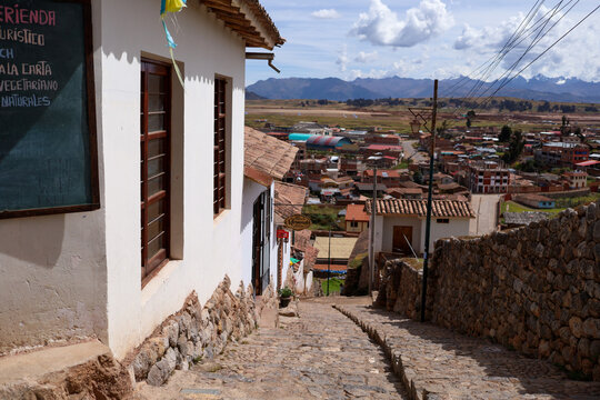 View of Chinchero with its traditional cobblestone street, white colonial buildings, and stone walls overlooking the town and Andean mountains in Cusco, Cusco, Peru.