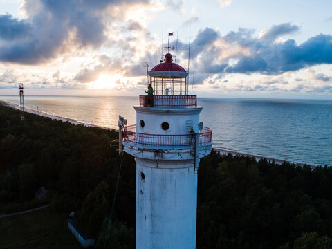 Mikeltornis, Latvia - 18 August 2018: Aerial view of the historic Mikelbaka lighthouse at sunset, with the Baltic Sea coastline and surrounding forest visible in the background.