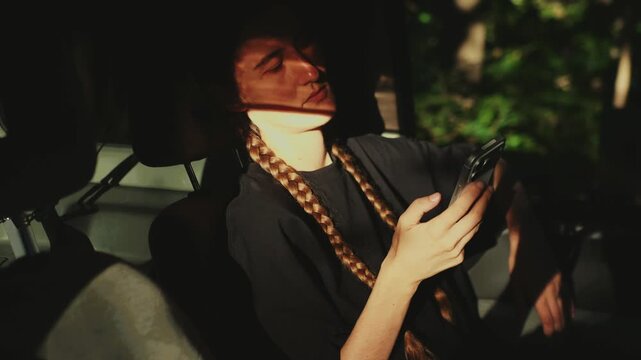 Woman using smartphone inside a sunlit car, representing mobile automotive service, booking apps, connected travel, and digital mobility business.