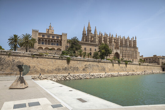 View of the historic Palma Cathedral and the Royal Palace of La Almudaina rising above the stone fortifications along the waterfront in Palma, Balearic Islands, Spain.