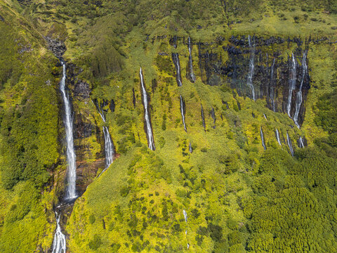 Aerial view of multiple waterfalls cascading down a lush green cliffside in the Azores, Portugal.
