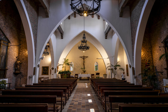 View of the interior of the Church of Saint Ramon of Penyafort with wooden pews, gothic arches, stone walls, and a crucifix at the altar in Port de Soller, Balearic Islands, Spain.
