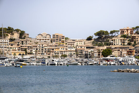 View of Port de Soller harbor with numerous moored boats and yachts against a backdrop of hillside buildings and lush trees in Port de Soller, Balearic Islands, Spain.