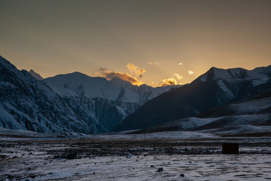 View of the Khunjerab Check Post area at sunset with snow-covered Karakoram mountain peaks, rocky terrain, and golden light on clouds in Hunza, Gilgit, Pakistan.
