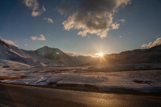 View of the sunset over the snow-capped peaks of the Karakoram mountains near the Khunjerab Pass, with the Karakoram Highway visible in the foreground in Hunza, Gilgit, Pakistan.
