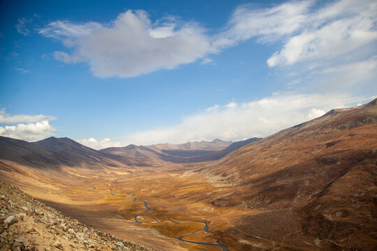 View of the winding stream flowing through the golden valley of Babusar Top surrounded by rugged mountain slopes under a bright blue sky in Babusar, KPK, Pakistan.