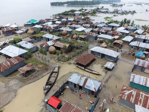Kurigram, Rangpur Division, Bangladesh - 06 July 2024: Aerial view of a flooded village with houses surrounded by rising water, wooden boats, and metal rooftops.