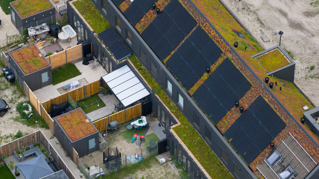 Aerial view of modern residential buildings featuring green roofs integrated with solar panels, private gardens, and patios in Almere, Flevoland, Netherlands.