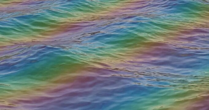 Colorful iridescent oil slick on wavy ocean surface