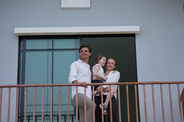 Obraz premium Happy young family with little daughter greet the neighborhood from the balcony with their daughter on the upper balcony of their new home above the neighborhood, shallow depth of field