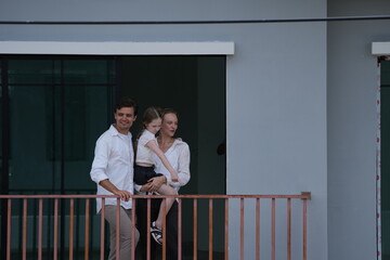 Obraz premium Young parents holding their child greet the neighborhood from the balcony with their daughter on the balcony of their new house overlooking the residential estate