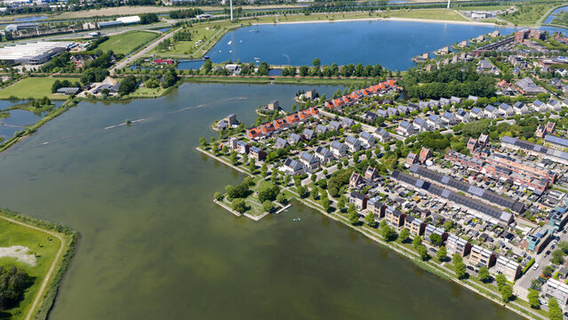Aerial view of a modern residential neighborhood with rows of houses, solar panels, and green spaces situated along a large lake in Heerhugowaard, North Holland, Netherlands.
