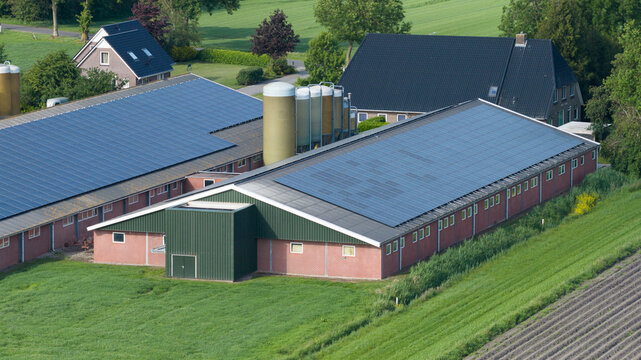 Aerial view of a farm with large barns featuring solar panels on the roofs, silos, and surrounding green agricultural fields in Giethoorn, Overijssel, Netherlands.