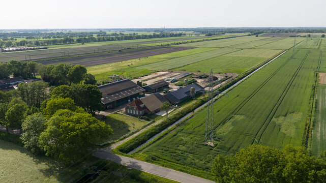 Aerial view of a traditional Dutch farm with barns and outbuildings surrounded by lush green agricultural fields, meadows, and drainage canals in Giethoorn, Overijssel, Netherlands.