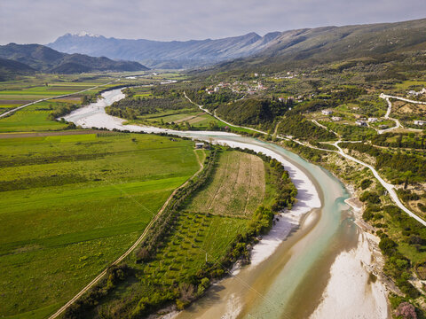 Aerial view of the Drashovica river landscape featuring winding riverbanks, lush green agricultural fields, and rolling hills in the background in Drashovica, Vlores, Albania.