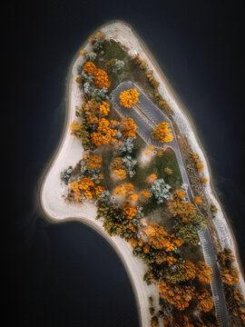 Aerial view of a peninsula with vibrant autumn foliage, a parking lot, and a sandy shoreline surrounded by dark water in Utah, United States.