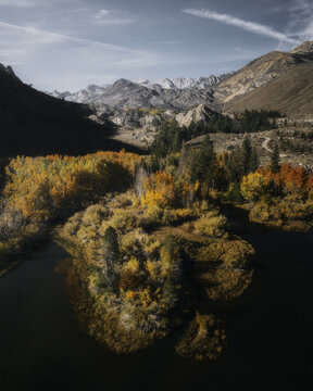 Aerial view of vibrant autumn foliage surrounding a mountain lake with rugged peaks in the background in Bishop, California, United States.